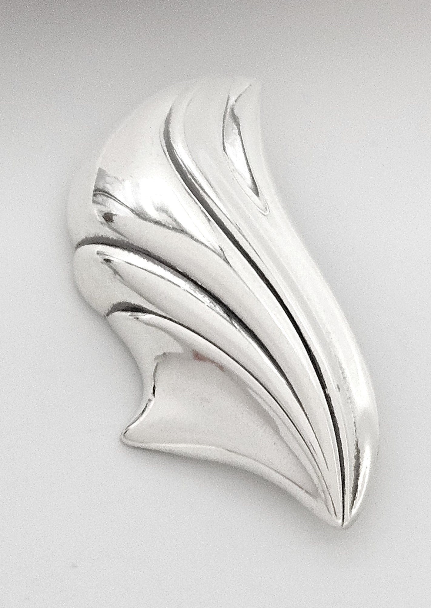 Silver brooch with a leaf-like design on a light gray background