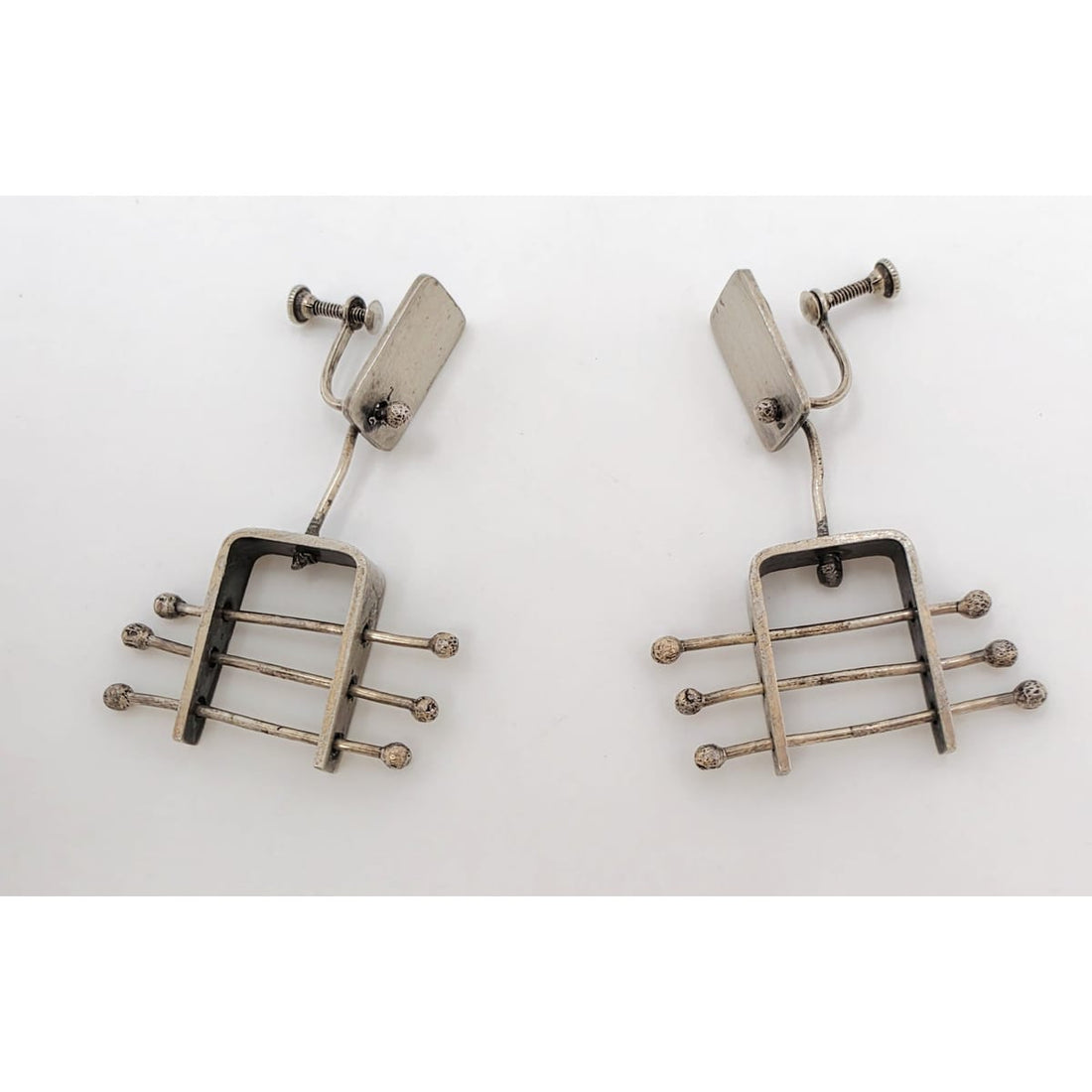 A pair of vintage silver-toned drop earrings with a geometric, guitar-fret-like design featuring horizontal bars and small round tips, photographed on a plain white background.