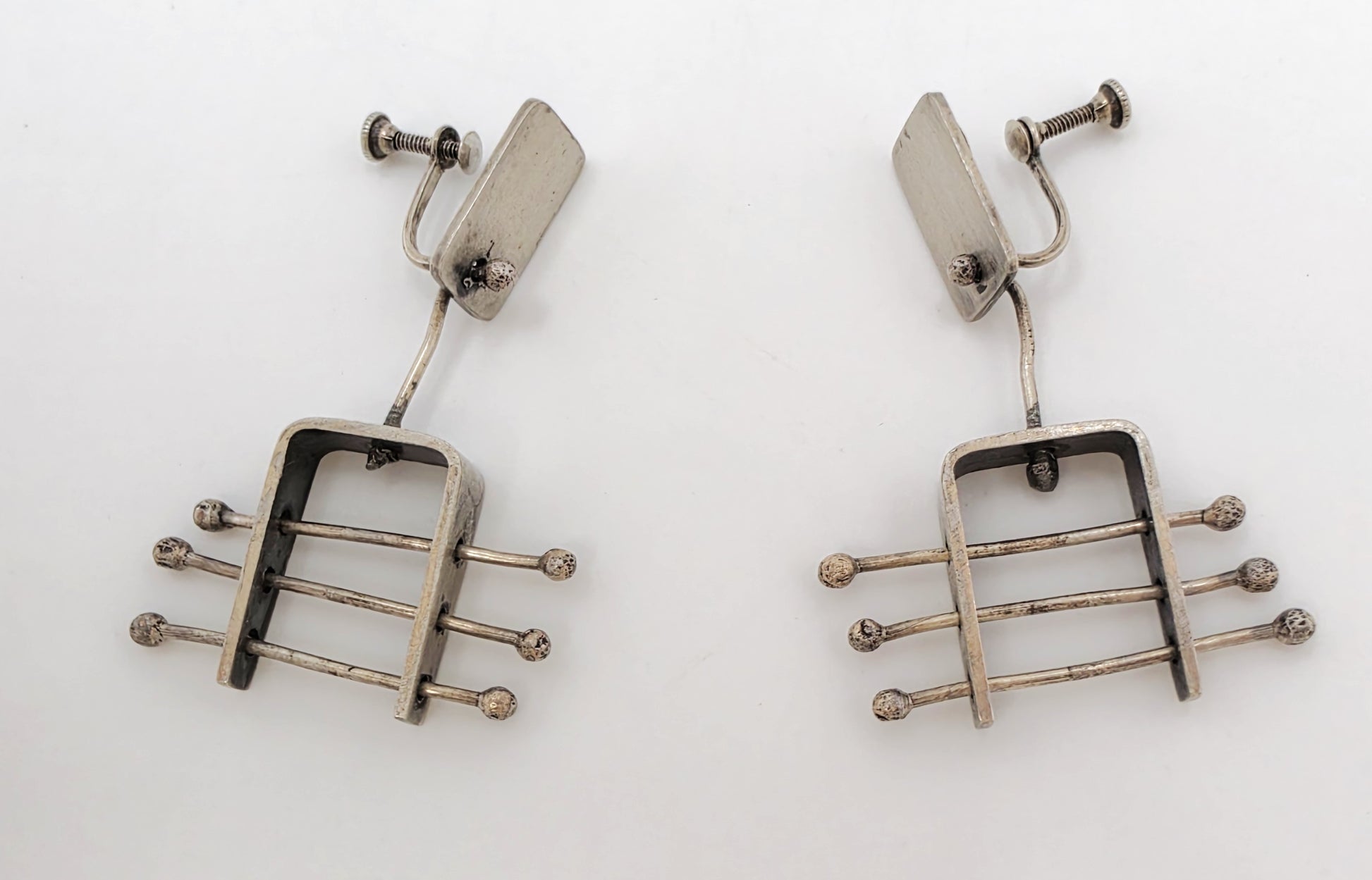 A pair of vintage silver-toned drop earrings with a geometric, guitar-fret-like design featuring horizontal bars and small round tips, photographed on a plain white background.